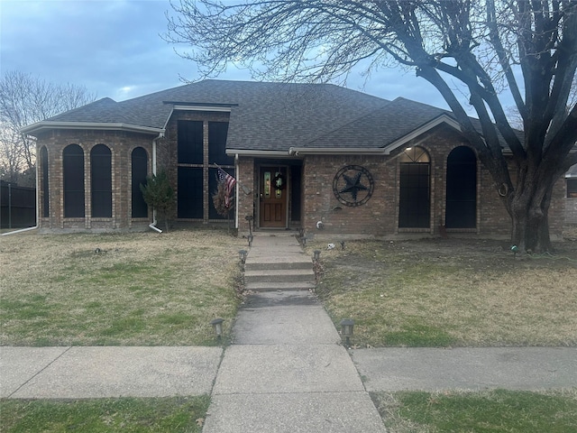 view of front of property featuring brick siding, roof with shingles, and a front yard