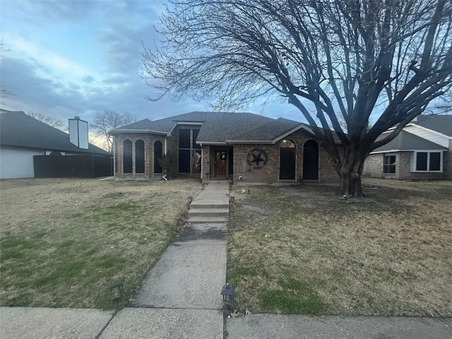 view of front facade featuring a front yard, brick siding, and roof with shingles