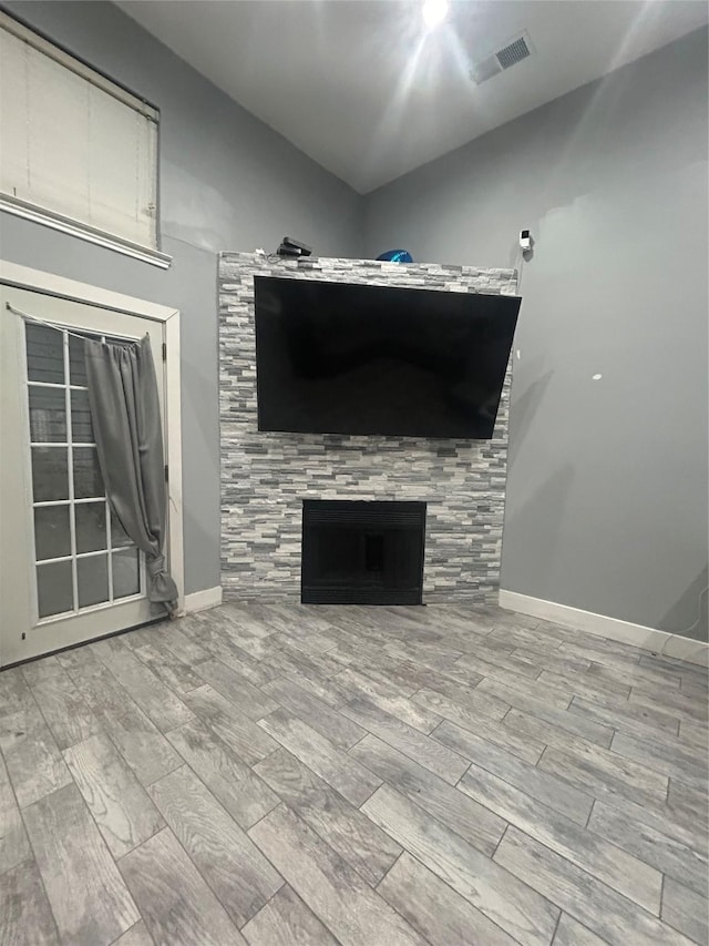 unfurnished living room featuring baseboards, visible vents, a tiled fireplace, lofted ceiling, and wood finish floors