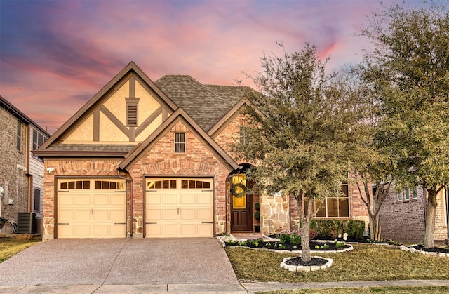 tudor-style house featuring a garage, concrete driveway, roof with shingles, cooling unit, and stucco siding