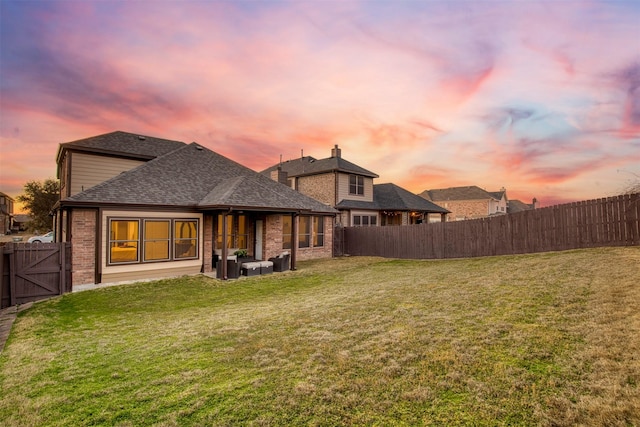 back of property featuring brick siding, a lawn, a shingled roof, and a fenced backyard