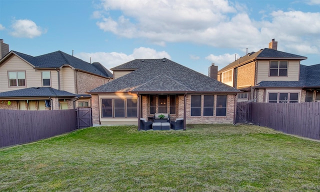 back of house featuring a gate, brick siding, a yard, and a fenced backyard