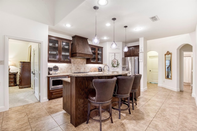 kitchen with arched walkways, stainless steel appliances, visible vents, dark brown cabinetry, and premium range hood