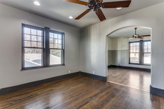 unfurnished room with dark wood finished floors, recessed lighting, arched walkways, baseboards, and ceiling fan