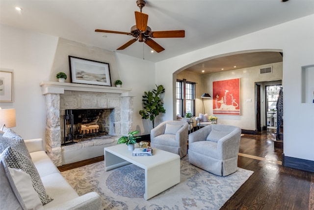 living room with arched walkways, recessed lighting, visible vents, a stone fireplace, and wood finished floors