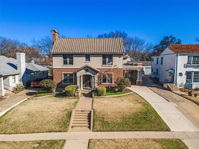 view of front of property featuring brick siding, a tiled roof, a chimney, and a front yard