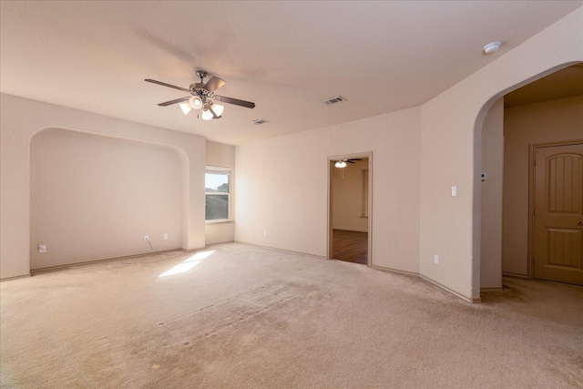 empty room featuring a ceiling fan, arched walkways, light colored carpet, and visible vents