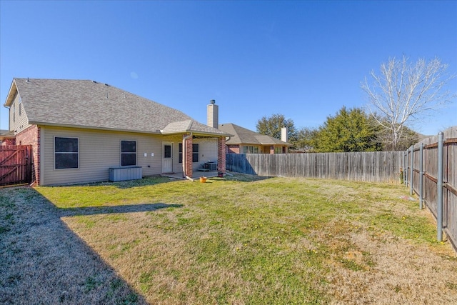 rear view of property with a fenced backyard, a yard, a chimney, and brick siding