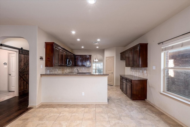 kitchen featuring dark brown cabinetry, a barn door, tasteful backsplash, arched walkways, and stainless steel microwave