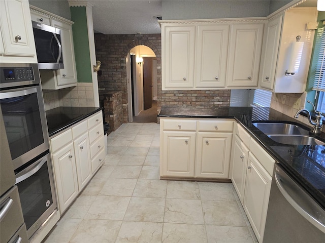 kitchen featuring arched walkways, stainless steel appliances, brick wall, a sink, and decorative backsplash