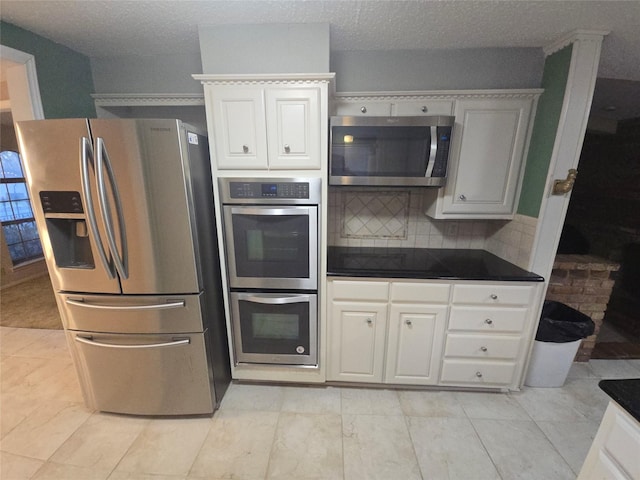 kitchen with tasteful backsplash, dark countertops, appliances with stainless steel finishes, white cabinets, and a textured ceiling