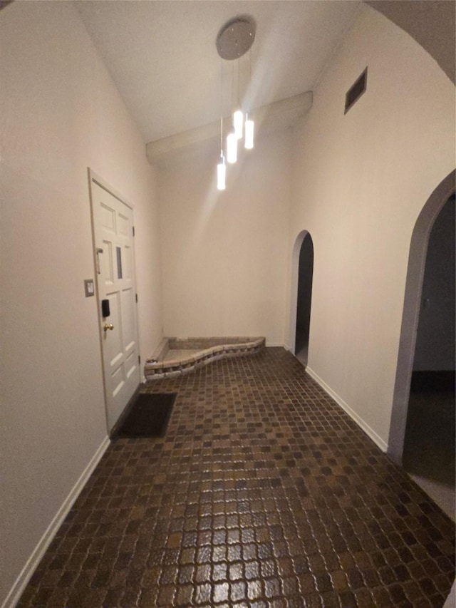 corridor featuring brick floor, visible vents, arched walkways, and baseboards