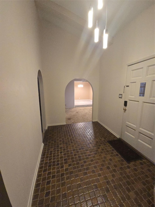 foyer entrance with a towering ceiling, brick floor, baseboards, and arched walkways