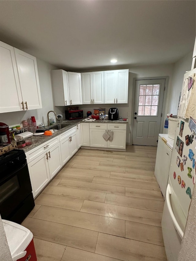 kitchen featuring light wood-type flooring, white cabinets, a sink, and black stove