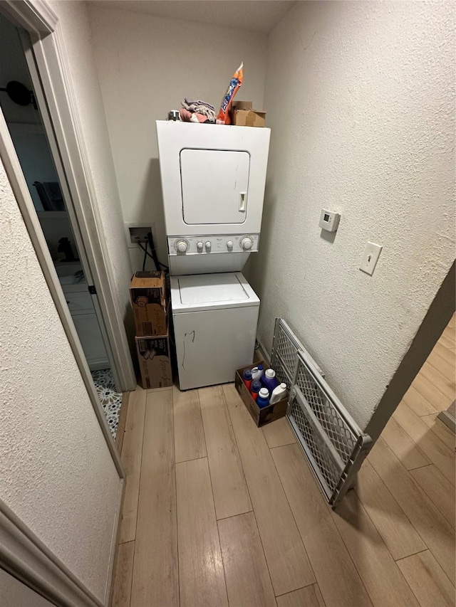 laundry room featuring light wood-type flooring, stacked washer and clothes dryer, a textured wall, and laundry area