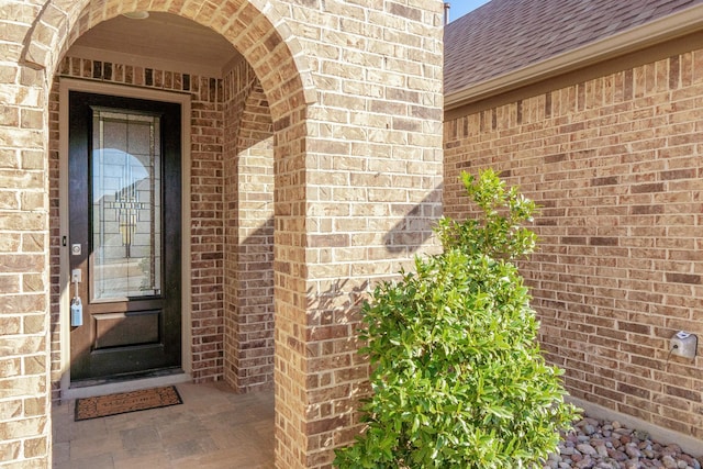 doorway to property with a shingled roof and brick siding