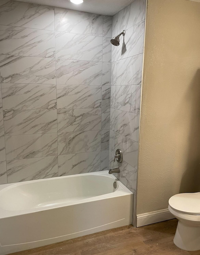 bathroom with a textured wall, toilet, wood finished floors, baseboards, and  shower combination