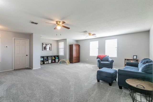 living room with a textured ceiling, visible vents, a ceiling fan, and light colored carpet