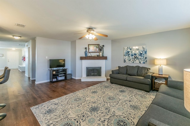 living room with visible vents, baseboards, dark wood finished floors, a ceiling fan, and a brick fireplace