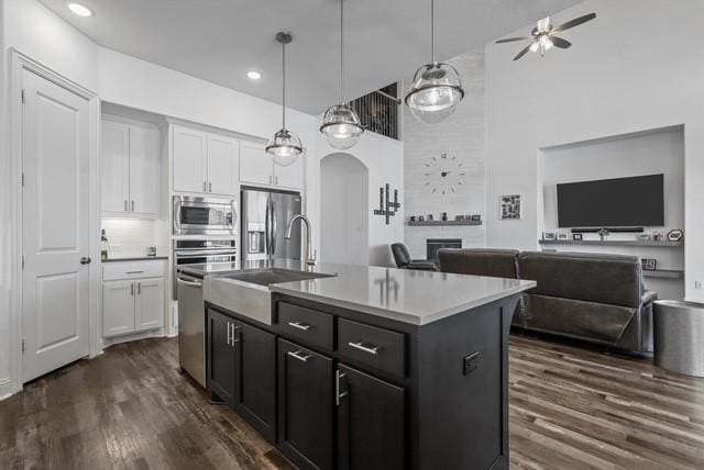 kitchen with arched walkways, open floor plan, dark wood-style flooring, stainless steel appliances, and a sink