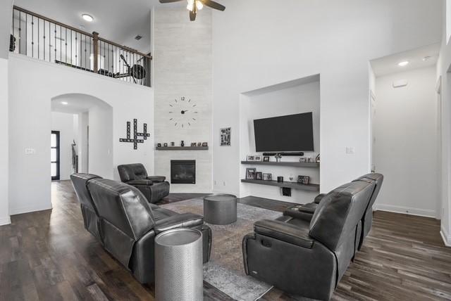 living area featuring arched walkways, ceiling fan, dark wood-type flooring, and a tile fireplace