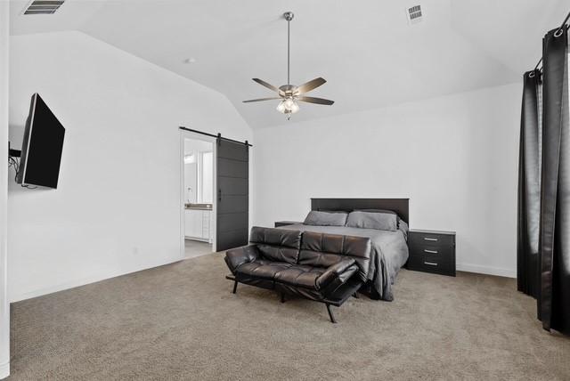 carpeted bedroom with lofted ceiling, a barn door, visible vents, and connected bathroom