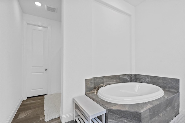 bathroom with wood finished floors, a garden tub, visible vents, and baseboards