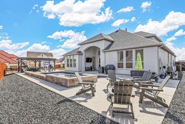 rear view of property featuring a patio, roof with shingles, an outdoor hot tub, and stucco siding