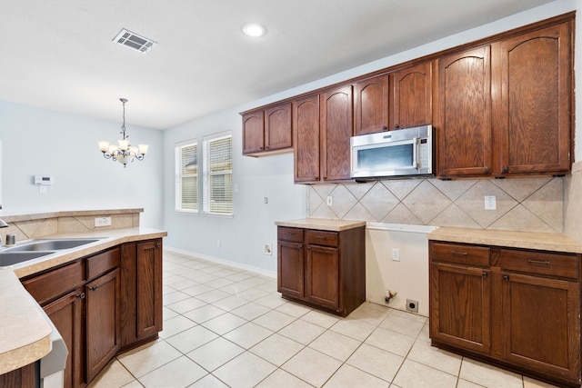 kitchen featuring light countertops, stainless steel microwave, backsplash, visible vents, and a sink