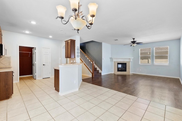 unfurnished living room with ceiling fan with notable chandelier, light tile patterned floors, a tiled fireplace, and stairs