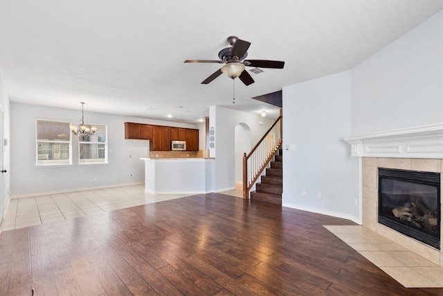 unfurnished living room with ceiling fan with notable chandelier, a fireplace, baseboards, and light wood-style floors