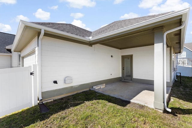 doorway to property featuring a garage, a shingled roof, and fence