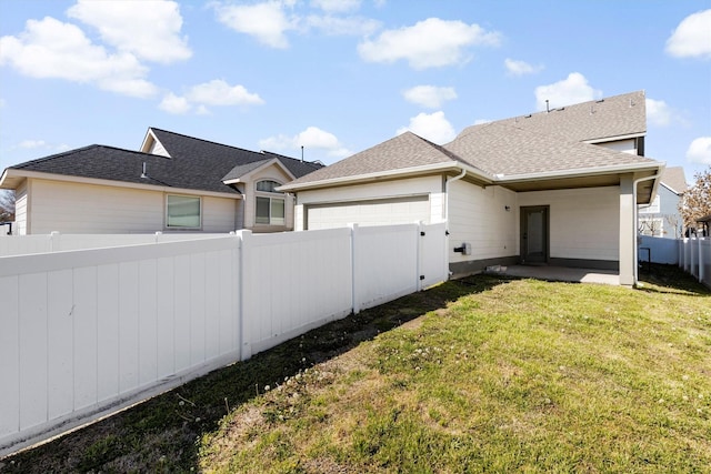 rear view of property with a shingled roof, a lawn, a fenced backyard, an attached garage, and a patio area