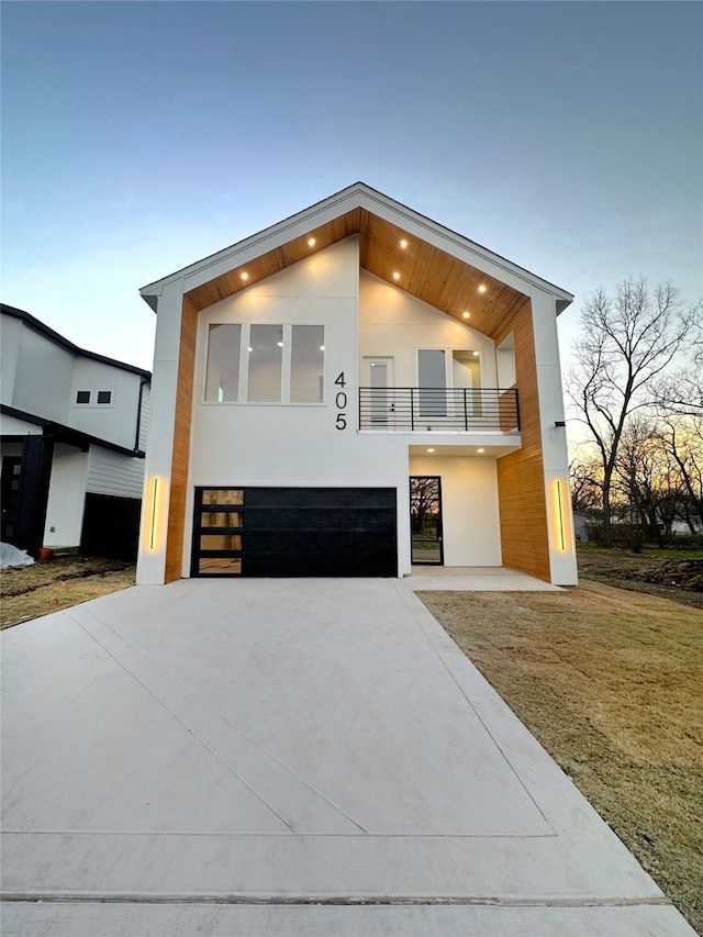 modern home with a balcony, driveway, an attached garage, and stucco siding