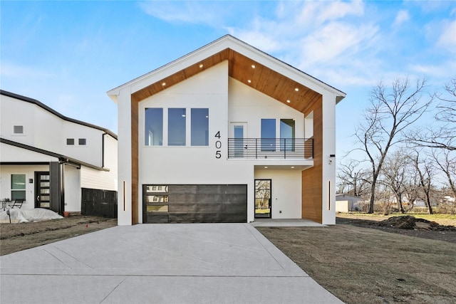 modern home featuring a garage, concrete driveway, a balcony, and stucco siding