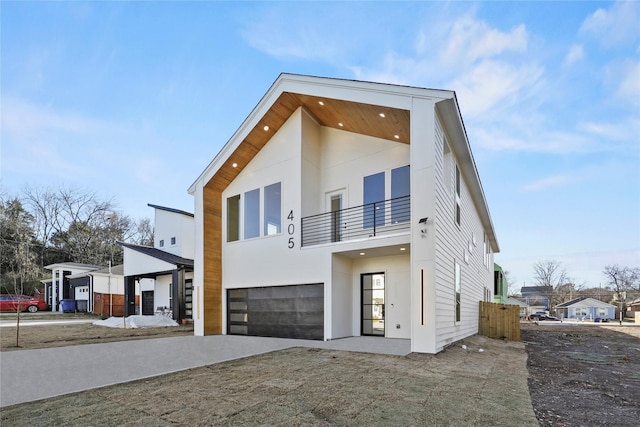 contemporary home with a garage, driveway, a balcony, and stucco siding