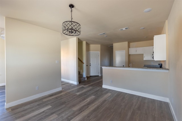 kitchen featuring light stone counters, dark wood-style flooring, white cabinets, a peninsula, and baseboards