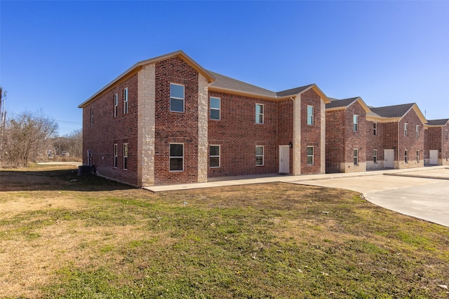 view of side of home featuring driveway, central AC unit, a lawn, a patio, and brick siding