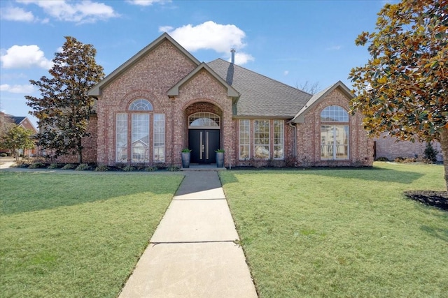 view of front of house featuring brick siding, a front lawn, and roof with shingles