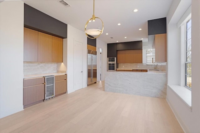 kitchen with wine cooler, pendant lighting, visible vents, light wood-style floors, and stainless steel double oven