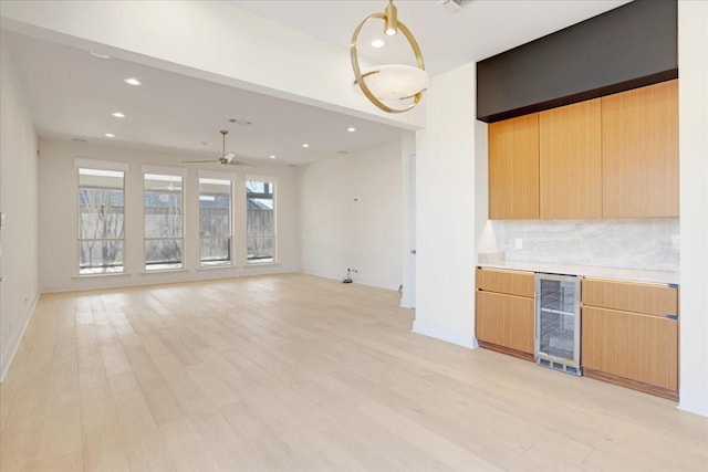 kitchen with wine cooler, light countertops, light wood-style flooring, backsplash, and open floor plan