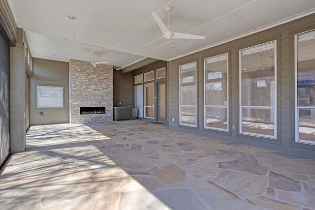 unfurnished sunroom with an outdoor stone fireplace and a ceiling fan