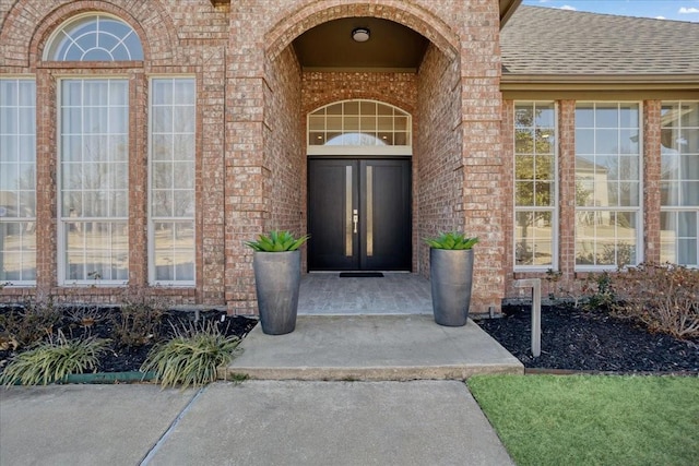 property entrance featuring a shingled roof and brick siding