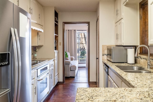 kitchen with white cabinets, light stone countertops, stainless steel appliances, and a sink