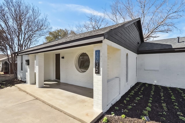 exterior space featuring a shingled roof and brick siding