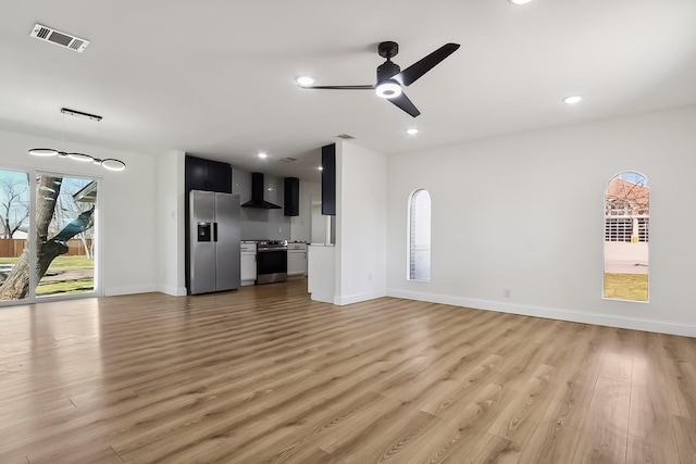 unfurnished living room with a healthy amount of sunlight, a ceiling fan, visible vents, and light wood-style floors