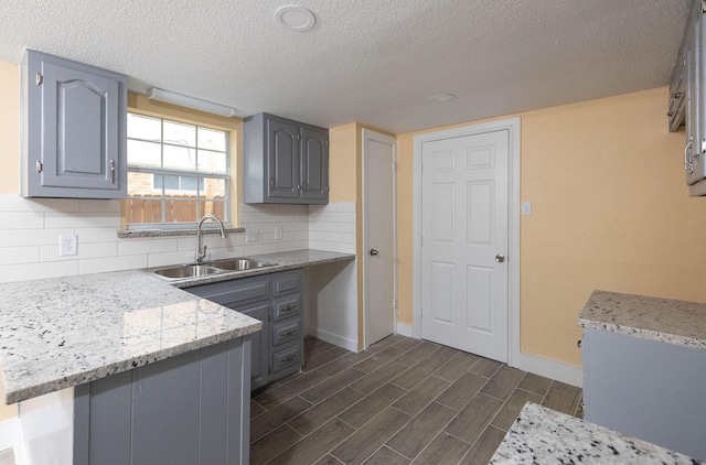 kitchen featuring light stone counters, backsplash, gray cabinetry, wood tiled floor, and a sink