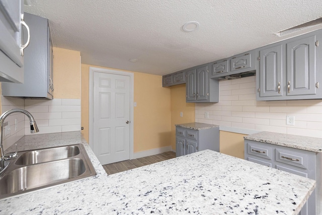 kitchen with light wood finished floors, light countertops, gray cabinetry, a sink, and a textured ceiling