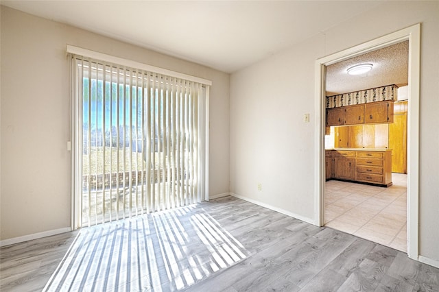 empty room featuring a textured ceiling, light wood finished floors, and baseboards