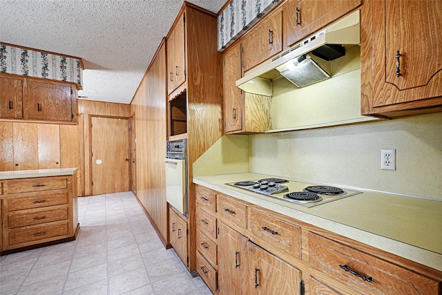 kitchen featuring under cabinet range hood, light countertops, white appliances, and brown cabinetry